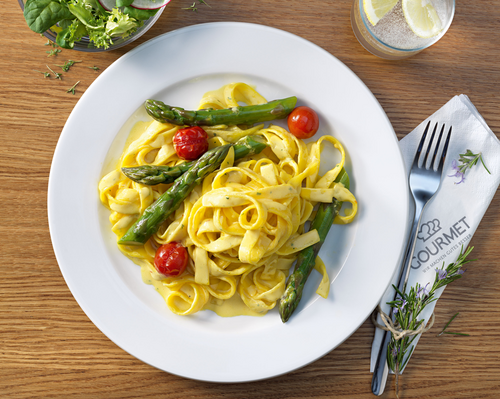 Spargel-Tagliatelle angerichtet auf einem Teller mit Besteck und Beilagensalat