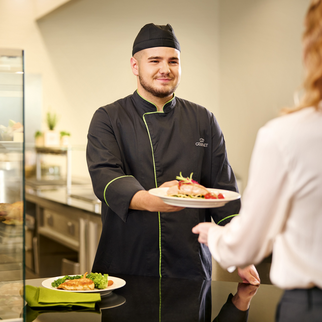 Koch serviert einer Person das Mittagessen angerichtet auf einem Teller